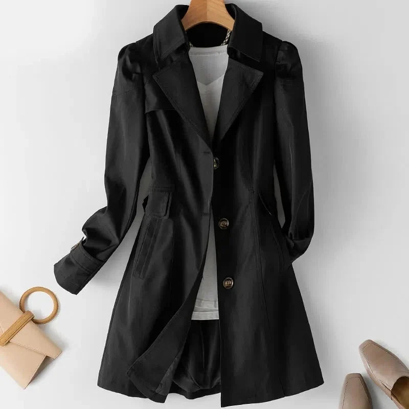 Black Novelle trench coat by Jack Hafford hanging on a wooden hanger, showing its classic double-breasted design and belt details.