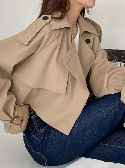 Women's cropped double-breasted trench coat by Homixa with lapels and adjustable cuffs, shown hanging on a neutral background.