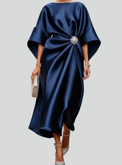 Women's satin midi dress by Homixa featuring draped fabric, batwing sleeves, and a waist brooch, shown on a model.