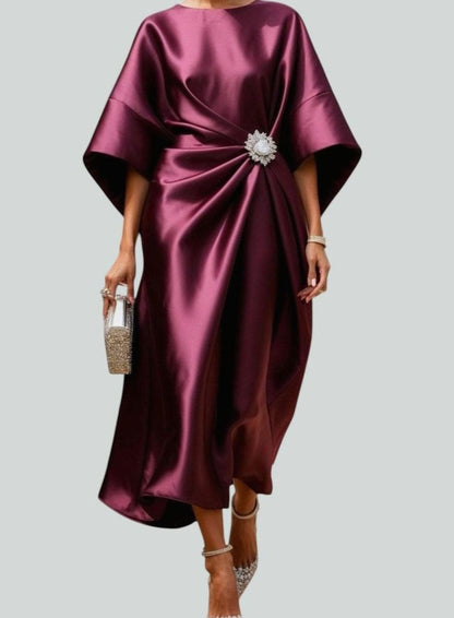 Women's satin midi dress by Homixa featuring draped design, batwing sleeves, and decorative brooch detail.