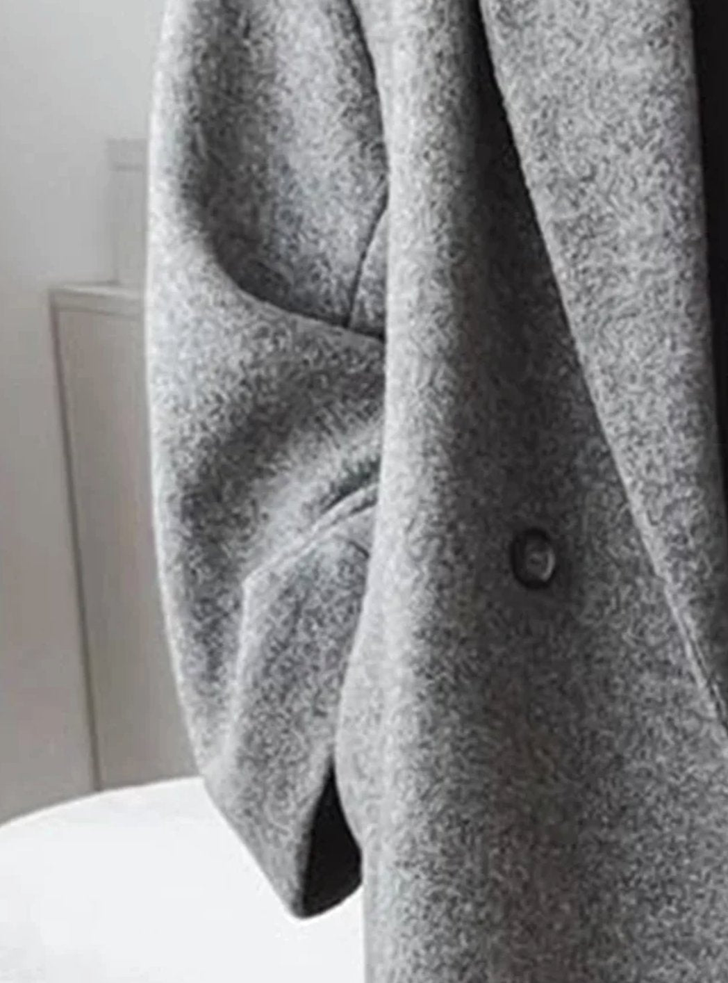 Women's oversized long wool coat by Homixa with lapels and two deep patch pockets, shown hanging on a wooden hanger.